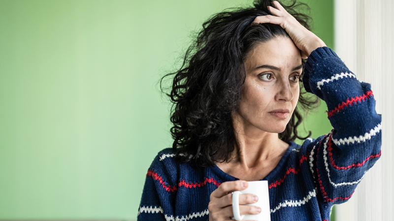 Mulher desempregada com uma caneca na mão e um ar preocupado